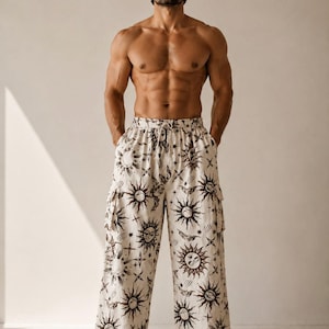 Peut inclure: Pantalon crème avec un motif répété de soleil et d'étoiles. Le pantalon a une taille à cordon et des poches cargo. Le motif présente des soleils avec des visages et divers éléments célestes.
