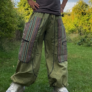 May include: Olive green trousers with patterned pockets. The trousers have a drawstring waist and a relaxed fit. The pockets feature a colourful striped design with black zips. The trousers are made of a lightweight fabric.
