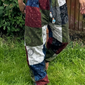 Puede incluir: Pantalones de patchwork con un dise&ntilde;o multicolor con cuadrados de tela azul, roja, verde y blanca. Cada cuadrado est&aacute; estampado con motivos celestiales que incluyen soles, lunas y estrellas. Los pantalones tienen una cintura el&aacute;stica con cord&oacute;n.