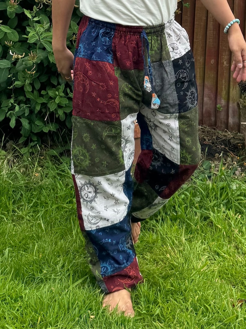 Puede incluir: Pantalones de patchwork con un dise&ntilde;o multicolor con cuadrados de tela azul, roja, verde y blanca. Cada cuadrado est&aacute; estampado con motivos celestiales que incluyen soles, lunas y estrellas. Los pantalones tienen una cintura el&aacute;stica con cord&oacute;n.