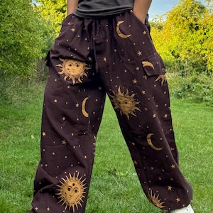 Può includere: Pantaloni marroni con un design celeste con soli, lune e stelle. I pantaloni hanno una vestibilità ampia con tasche e vita con coulisse. Le grafiche del sole e della luna sono dorate, creando un contrasto sorprendente.