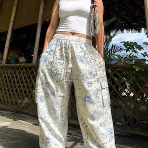 May include: A white ribbed vest top paired with loose-fitting, cream-coloured cargo trousers featuring an all-over blue print of suns, moons, and celestial patterns. The trousers include a drawstring waist and large side pockets on each leg.