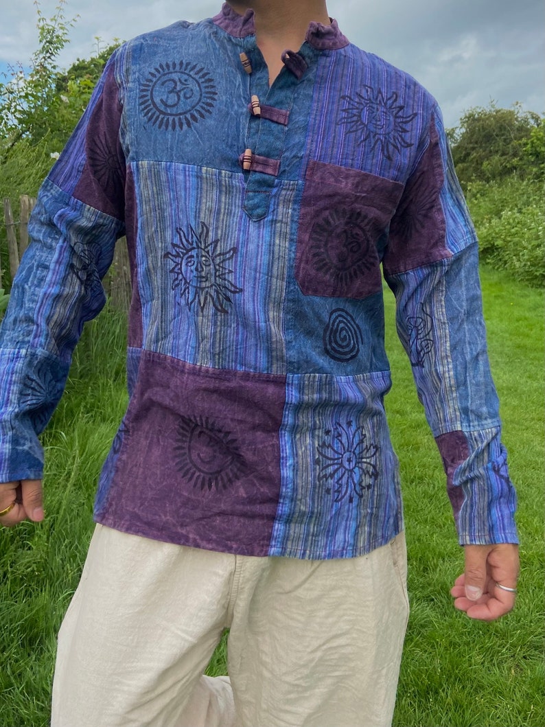 May include: A long-sleeved shirt with a patchwork design featuring various symbols and patterns, including suns, a spiral, and an Om symbol. The shirt is made of a soft, cotton fabric and has a relaxed fit.