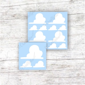 May include: Two square stickers with a light blue background and white cloud designs. The stickers feature various sizes of fluffy white clouds. The stickers are on a light wood grain surface.