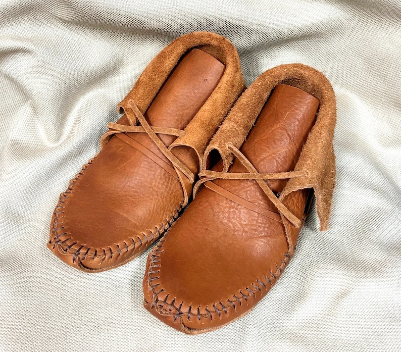Peut inclure: Une paire de mocassins en cuir marron avec des lacets. Les mocassins ont une doublure en daim et sont cousus avec un motif d&eacute;coratif.