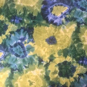 Op de afbeelding: Een tie-dye stof met een draaiende print in blauw, groen en geel.
