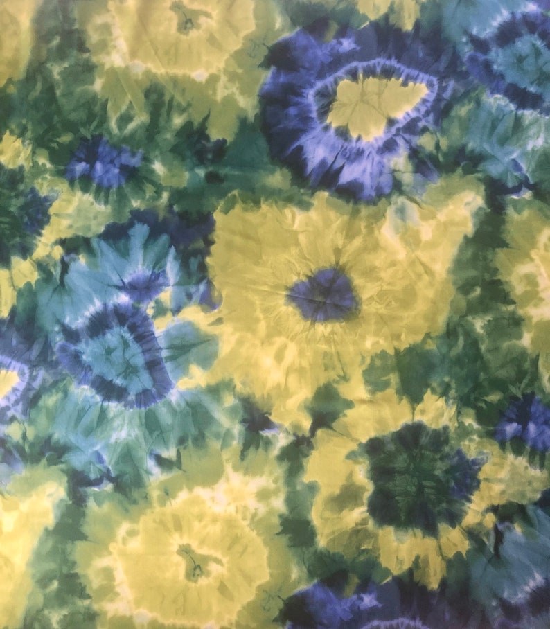 Op de afbeelding: Een tie-dye stof met een draaiende print in blauw, groen en geel.