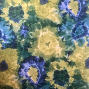 Op de afbeelding: Een tie-dye stof met een draaiende print in blauw, groen en geel.
