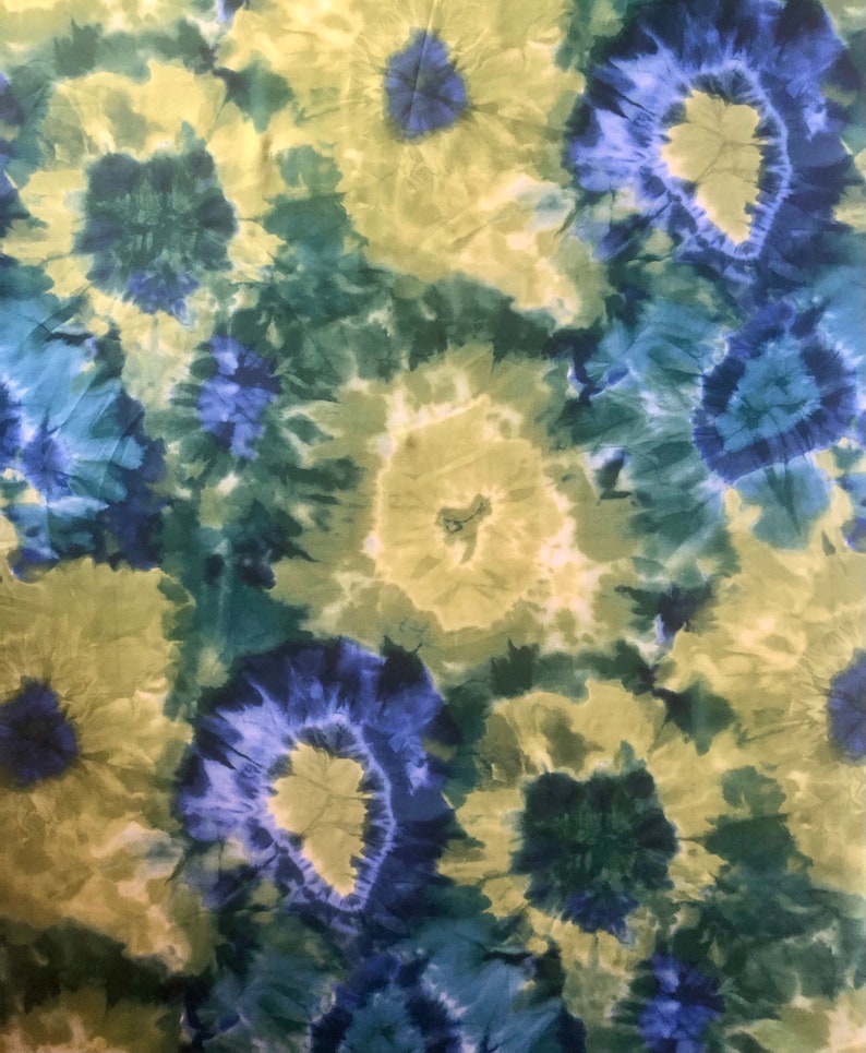 Op de afbeelding: Een tie-dye stof met een draaiende print in blauw, groen en geel.