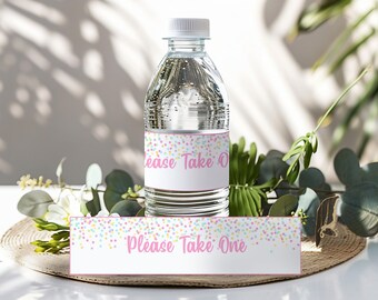 Könnte beinhalten: Eine durchsichtige Plastikwasserflasche mit einem rosa-weißen Etikett, auf dem "Bitte nehmen Sie eins" mit bunten Konfetti steht. Die Flasche steht auf einem braunen geflochtenen Untersetzer.