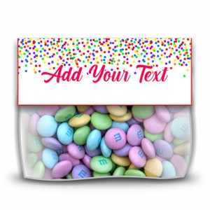 May include: A clear plastic bag filled with pastel-colored M&M's candies. The bag has a white label with a red border and the text "Add Your Text" in pink cursive writing. The label is decorated with a rainbow confetti pattern.