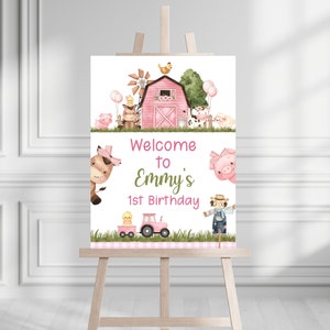 May include: Welcome to Emmy's 1st Birthday sign with a pink barn, farm animals, and a tractor. The sign is on a white background with green grass and pink and white checkered accents.