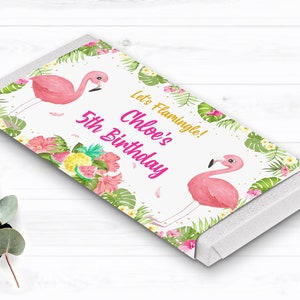 May include: A white chocolate bar wrapper with a pink flamingo, tropical leaves, and flowers. The text on the wrapper reads "Let's Flamingle! Chloe's 5th Birthday".