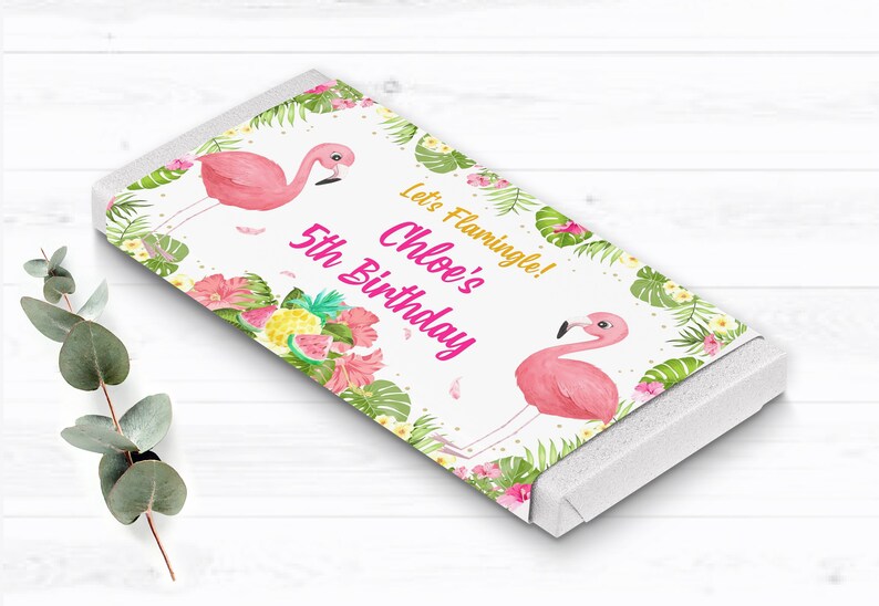 May include: A white chocolate bar wrapper with a pink flamingo, tropical leaves, and flowers. The text on the wrapper reads "Let's Flamingle! Chloe's 5th Birthday".