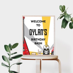 K&ouml;nnte beinhalten: Ein Willkommenszeichen f&uuml;r eine Geburtstagsparty mit Rock'n'Roll-Thema. Das Schild ist wei&szlig; mit schwarzem Text und zeigt eine rote E-Gitarre, einen Totenkopf mit Blitz und einen Lautsprecher. Der Text auf dem Schild lautet "Willkommen zu Dylans Geburtstagsfeier".