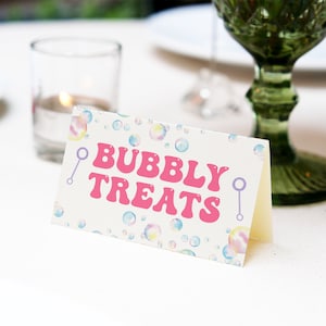 May include: A white card with a pastel rainbow bubble pattern and the text "Bubbly Treats" in pink letters. There are two purple and white bubble wands on either side of the text.