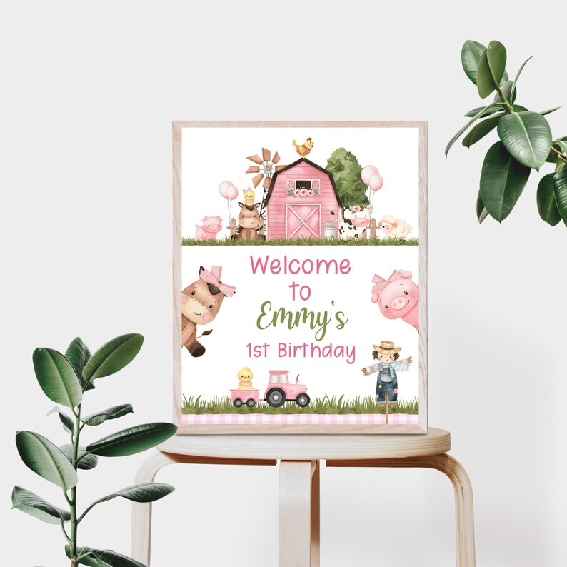 May include: A pink and white welcome sign with a farm theme. The sign features a pink barn, a cow, a pig, a chicken, a tractor, and a scarecrow. The text on the sign reads "Welcome to Emmy's 1st Birthday".