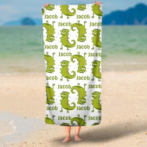 May include: White beach towel with a repeating pattern of green cartoon lizards and the name "Jacob" printed on the towel.