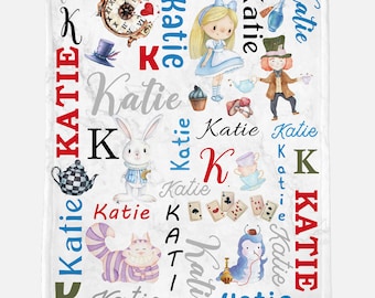 Op de afbeelding: Een wit gepersonaliseerd deken met een fantasierijk Alice in Wonderland-thema. Het deken bevat illustraties van Alice, de Hoedenmaker, de Cheshire Cat, het Witte Konijn en andere personages uit het verhaal. De naam "Katie" wordt herhaald in het hele ontwerp in verschillende kleuren en lettertypen.