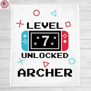 May include: White blanket with a video game controller design. The text reads "Level 7 Unlocked Archer" with pixelated font and colorful game icons.