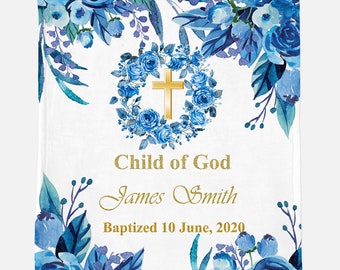 May include: A white baby blanket with a blue floral design. The blanket features a gold cross in a wreath of blue flowers. The text "Child of God" is written in gold script, followed by the name "James Smith" and the date "Baptized 10 June, 2020".