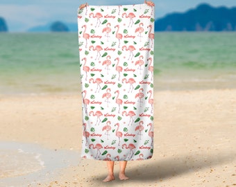 Op de afbeelding: Een witte strandhanddoek met een roze flamingo en groen bladpatroon. De naam "Lindsey" wordt herhaald in het hele patroon.
