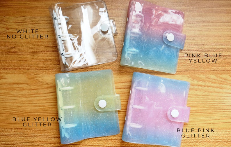 以下が含まれることがあります： 異なる色のグラデーションとグリッターが付いた透明なプラスチックバインダーが4つあります。バインダーには、「WHITE NO GLITTER」、「PINK BLUE YELLOW」、「BLUE YELLOW GLITTER」、「BLUE PINK GLITTER」とラベルが付けられています。