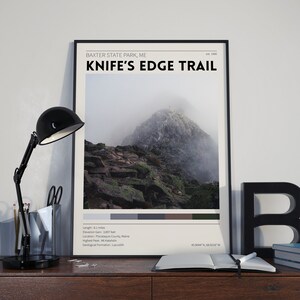 May include: A black and white poster with the text "Knife's Edge Trail" in a bold font. The poster also includes the text "Baxter State Park, ME" and "est. 1931". The poster features a photograph of a mountain peak with fog and clouds. The poster also includes the following information: Length: 8.1 miles, Elevation Gain: 3,897 feet, Location: Piscataquis County, Maine, Highest Peak: Mt Katahdin, Geological Formation: Laccolich, 45.9044°N, 68.9036°W.