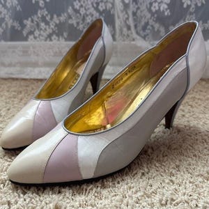 May include: A pair of vintage leather pumps in cream, light pink, and gray. The heels are dark brown, and the inner sole is gold. The shoes have a pointed toe and a classic design, perfect for a retro look.