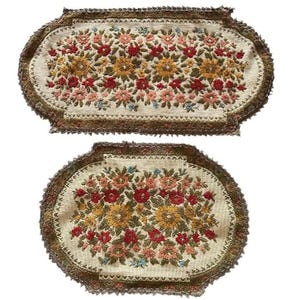 May include: Two oval-shaped embroidered pieces with floral designs. The pieces feature a cream-colored background with a variety of flowers in shades of red, yellow, pink, and blue. The edges are trimmed with a brown, textured border.