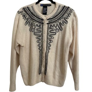 May include: Cream-colored cardigan sweater with black and gray embroidered design. The sweater has a button-up front and ribbed cuffs and hem. The label reads "IB DIFFUSION".