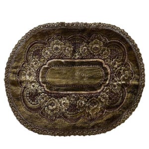 May include: An oval-shaped, olive green decorative mat with a floral pattern and a central rectangular design. The mat has a dark brown border and a scalloped edge, creating a vintage aesthetic.