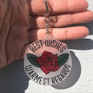 Schitts creek quote/ phrase “best wishes warmest regards” in black with red and green rosebud frosted 2 1/2 inch shrinky dink keychain