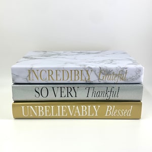 May include: A stack of three decorative books with gold, silver, and marble covers. The top book has the text "INCREDIBLY Grateful" in gold lettering. The middle book has the text "SO VERY Thankful" in black lettering. The bottom book has the text "UNBELIEVABLY Blessed" in white lettering.