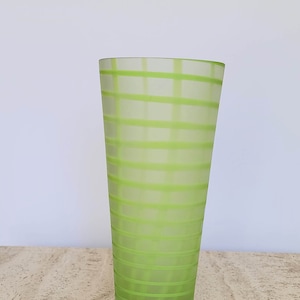 May include: A frosted green glass vase with a striped pattern. The vase is tall and slender, with a rounded base and a flared opening.