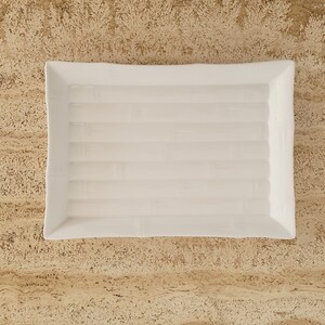 May include: A white rectangular ceramic serving dish with a textured, raised design that resembles bamboo.