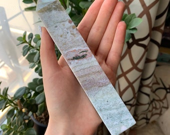 May include: A long, slender, white and green striped crystal wand with a pointed tip. The wand has a subtle pink and brown stripe running through the center.