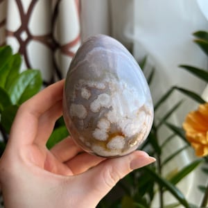 May include: A white and brown agate egg with a unique, swirling pattern. The egg is smooth and polished, with a light sheen.