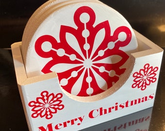 May include: Set of white ceramic coasters with a red snowflake design. The coasters are in a white wooden holder with the words "Merry Christmas" written on the front.