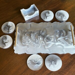 May include: A set of six silver and black coasters with a swirling design, a matching tray with a silver and black swirling design, and a small silver and black box.