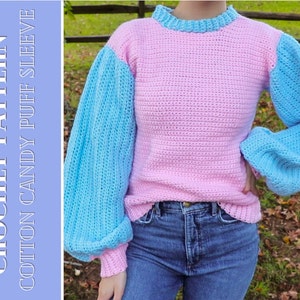 May include: A crochet sweater with a pink body and blue puff sleeves. The sweater has a round neckline and is made with a textured stitch.