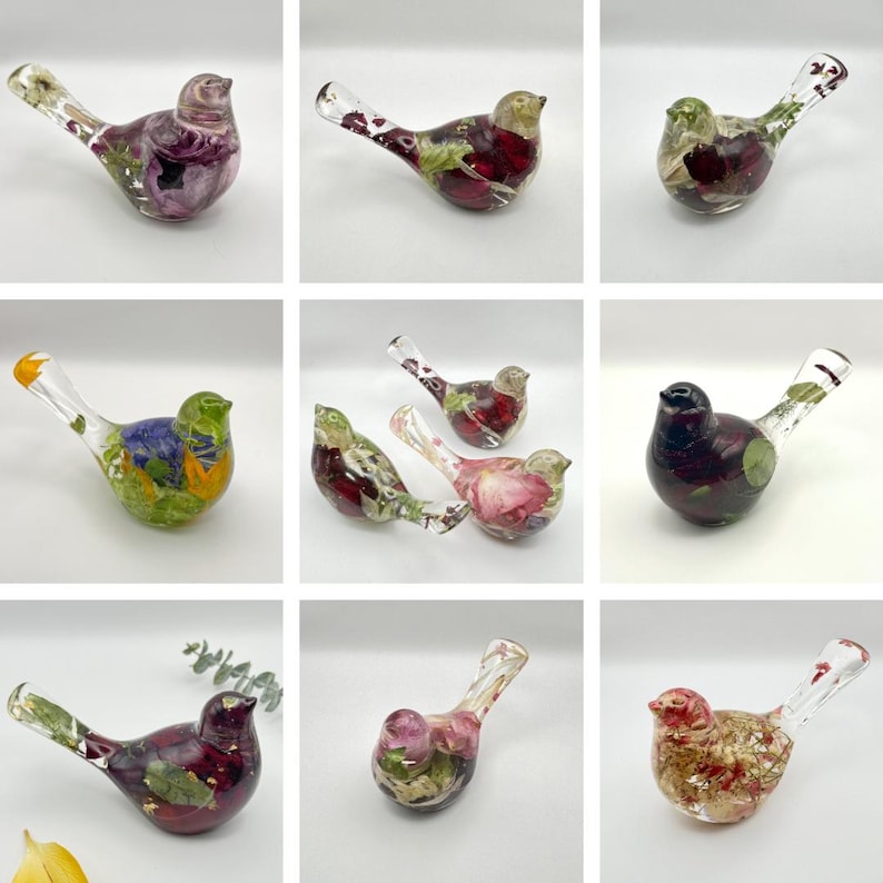 Op de afbeelding: Een verzameling decoratieve glazen vogelbeeldjes. Elke vogel is gevuld met kleurrijke gedroogde bloemen en bladeren, met een verscheidenheid aan tinten, waaronder rood, paars, groen en geel. De vogels hebben heldere glazen snavels en staarten.