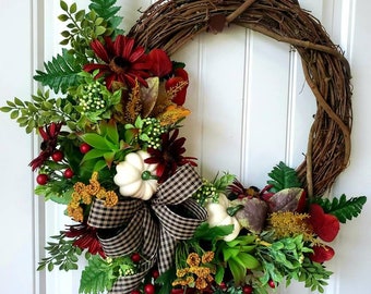 May include: A fall-themed wreath with a brown vine base, decorated with white pumpkins, red and green leaves, and a black and white checkered bow.
