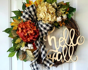 May include: A fall wreath with a black and white checkered ribbon, orange and cream hydrangeas, and a wooden sign that says "hello fall".