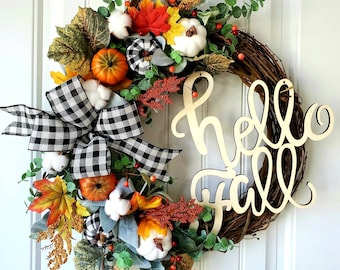 May include: A fall-themed wreath with a grapevine base, adorned with pumpkins, leaves, cotton, and a black and white checkered bow. The wreath includes the words "hello fall" in a wooden script. The color palette includes orange, white, green, and black.
