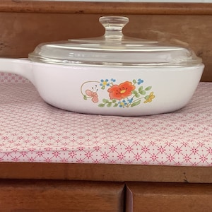May include: White ceramic casserole dish with a floral design featuring orange, pink, and blue flowers. The dish has a clear glass lid.