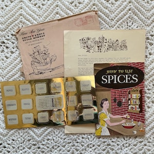 May include: A collection of vintage spice-related ephemera, including a booklet titled "How to Use Spices," a sheet of gold-colored spice labels, and a pamphlet with a ship illustration. The items are arranged on a white crocheted surface.