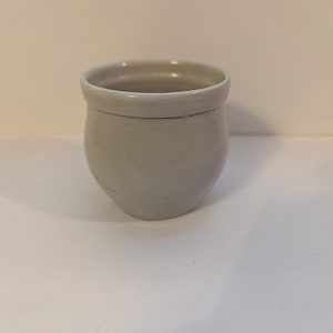 May include: A small, white ceramic cup with a rounded bottom and a slightly flared rim.