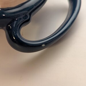 May include: Close-up of a blue ceramic mug handle with a white speck on the surface.