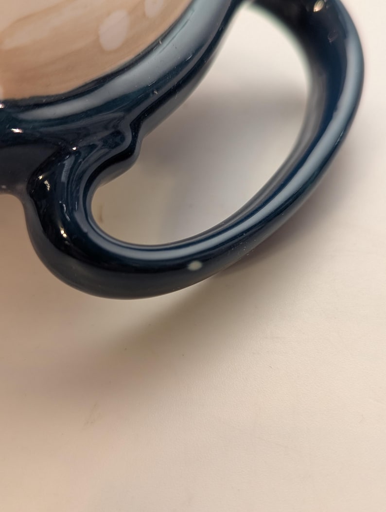 May include: Close-up of a blue ceramic mug handle with a white speck on the surface.